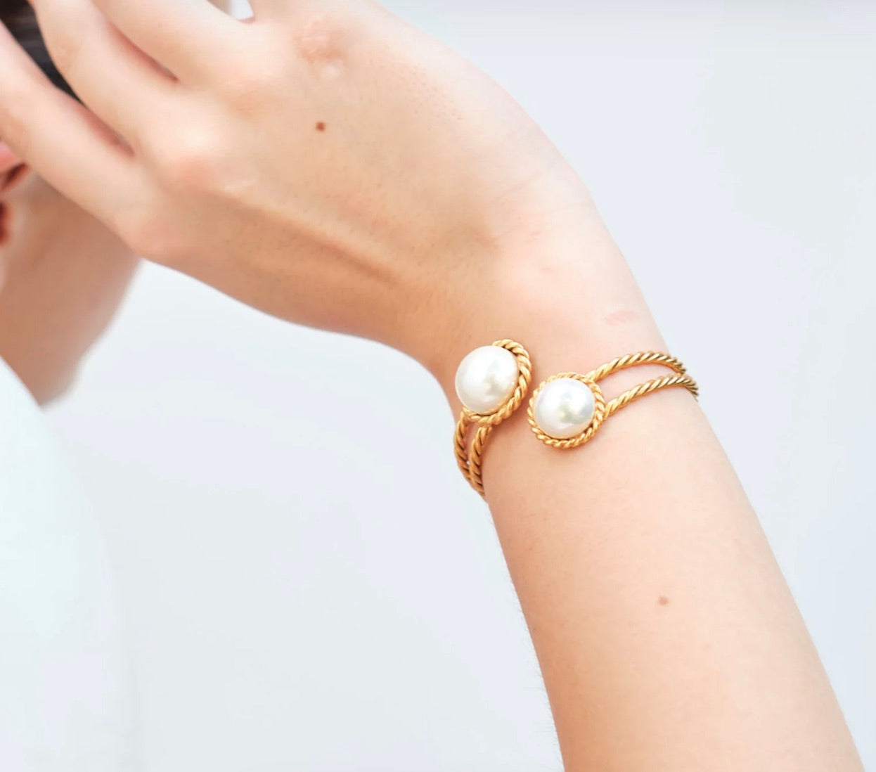 A person's arm showcasing a gold-plated brass cuff bracelet with two white pearls.