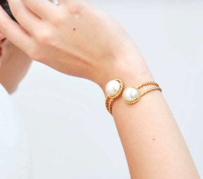 A person's arm showcasing a gold-plated brass cuff bracelet with two white pearls.